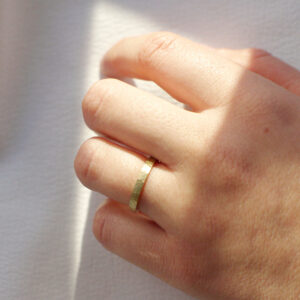 Mão feminina usando Aliança minimalista de 2,5mm de textura martelada feita a mão em ouro 18k