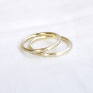 Par de alianças de aro redondo 1,8mm com diamantes minimalistas feitas a mão em ouro 18k para casamentos sobre tecido branco