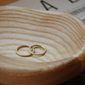 Par de alianças de aro redondo 1,8mm com diamantes minimalistas feitas a mão em ouro 18k para casamentos sobre superfície de madeira