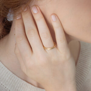 Mulher usando Aliança de aro redondo 2,4mm minimalista feita a mão em ouro 18k para casamentos sobre fundo branco