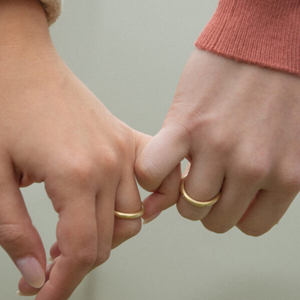 Mão de casal usando Alianças de aro redondo 2,4mm minimalistas feitas a mão em ouro 18k para casamentos