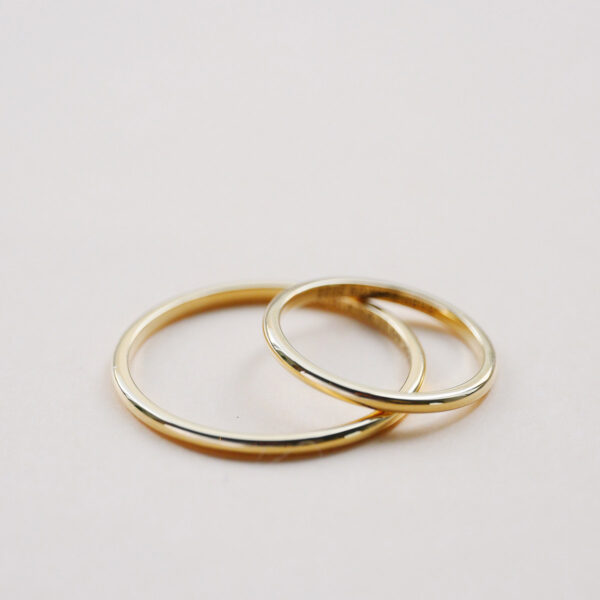 Par de Alianças meia cana com aro de 1,5mm finas minimalistas feitas a mão em ouro 18k para casamentos sobre fundo branco
