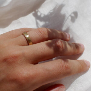 Mão feminina usando Aliança de casamento feita a mão em ouro 18k facetada minimalista sobre tecido branco