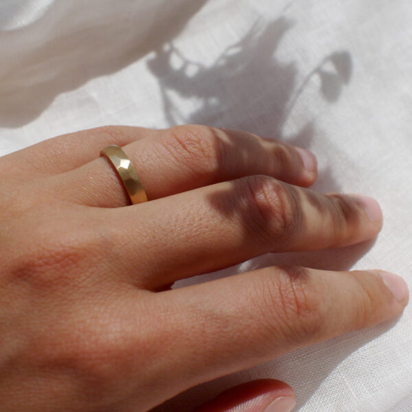 Mão feminina usando Aliança de casamento feita a mão em ouro 18k facetada minimalista sobre tecido branco