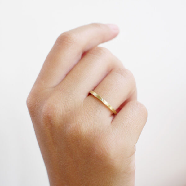 mão feminina com aliança fina de casamento feita a mão em ouro 18k e diamante central minimalista
