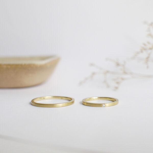 par de alianças finas de casamento feitas a mão em ouro 18k e diamante central minimalistas sobre fundo branco