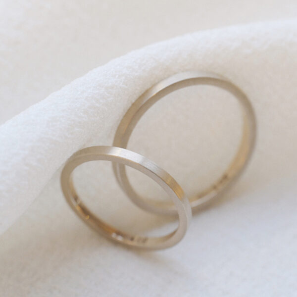 par de alianças de casamento finas feitas a mão em ouro 18k minimalistas sobre fundo branco