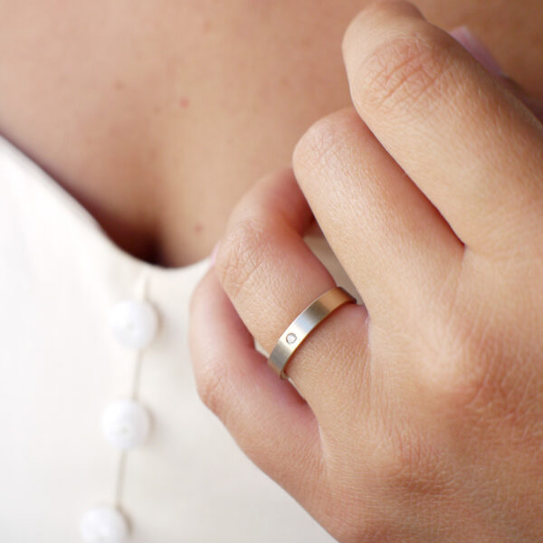 mão feminina com aliança fina de casamento feita a mão em ouro 18k e diamante central minimalista