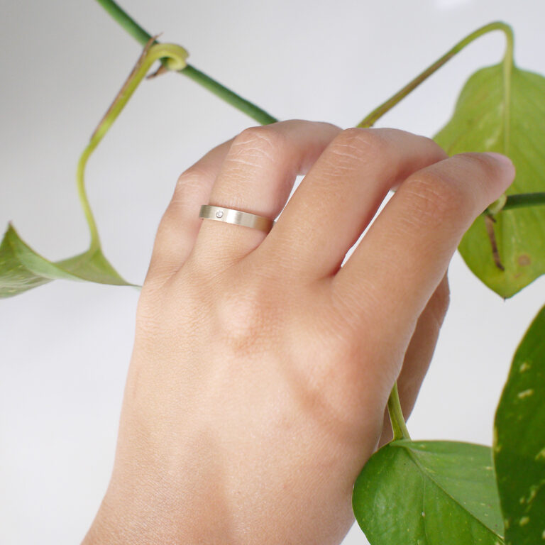 mão feminina com aliança fina de casamento feita a mão em ouro 18k e diamante central minimalista com planta