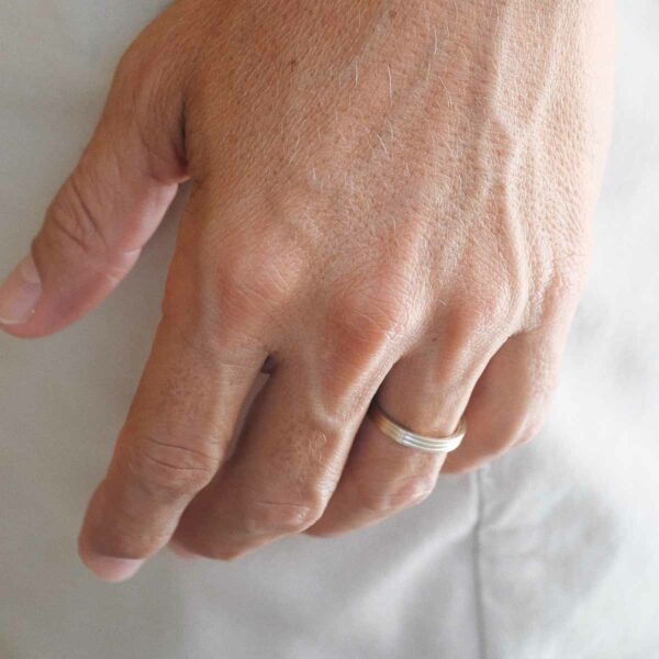 Mão masculina usando alinça de casamento feita a mão em ouro 18k com detalhes de linhas minimalista