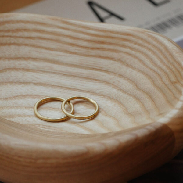 Par de alianças de aro redondo 1,8mm minimalistas feitas a mão em ouro 18k para casamentos sobre prato de madeira