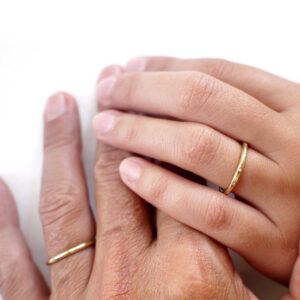 Casal usando par de alianças de aro redondo 1,8mm minimalistas feitas a mão em ouro 18k para casamentos sobre tecido branco