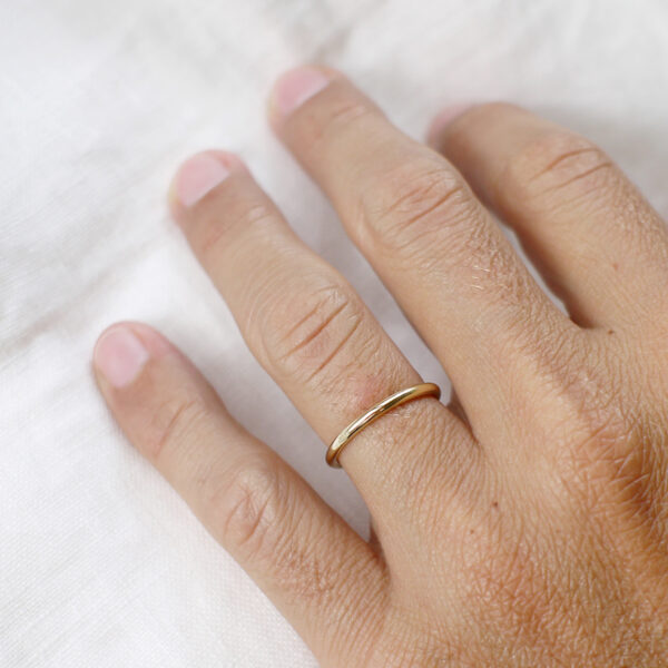 Mão masculina usando Aliança de aro redondo 1,8mm minimalista feita a mão em ouro 18k para casamentos sobre tecido branco