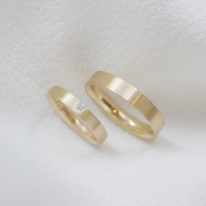 par de alianças de casamento feitas a mão em ouro 18k e diamante central de 3 pontos minimalistas sobre fundo branco