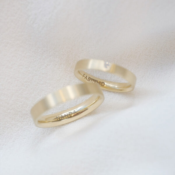 par de alianças de casamento feita à mão em ouro 18k e diamante central de 3 pontos minimalista e gravação sobre fundo branco