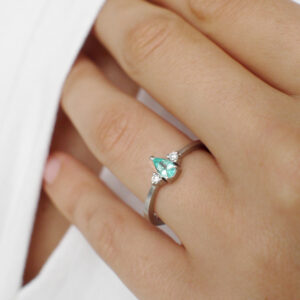 Mão feminina vestindo anel de noivado em ouro 18k branco com turmalina paraíba natural em formato de gota e dois diamantes