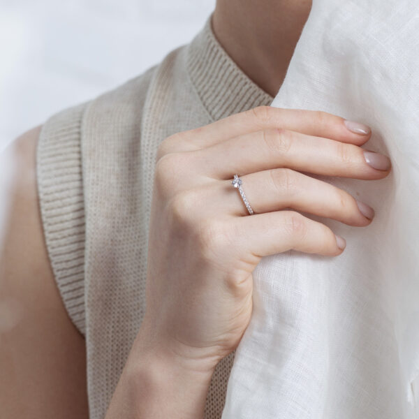 Mão feminina usando anel solitário cravejado minimalista de diamantes em ouro 18k
