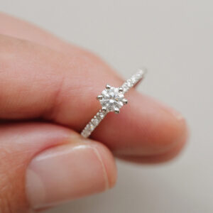 Mão segurando anel solitário cravejado minimalista de diamantes em ouro 18k