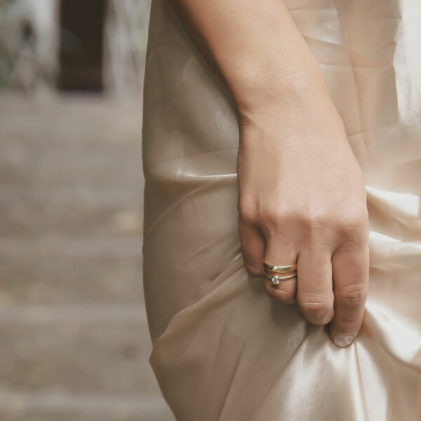 Mulher segurando o vestido usando Aliança minimalista feita a mão em ouro 18k com diamante para casamentos