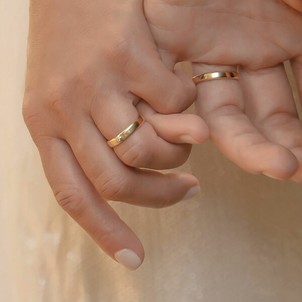 Mãos entrelaçadas usando Par de alianças minimalistas feitas a mão em ouro 18k com diamante para casamentos