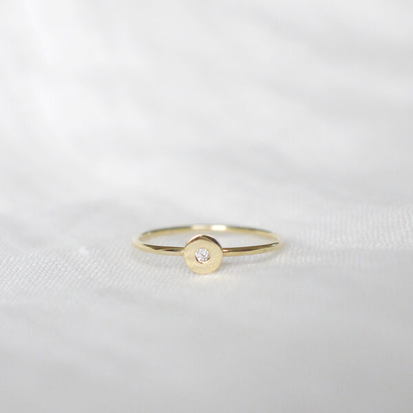 Anel de aro fino minimalista feito a mão em ouro 18k com diamante no centro sobre tecido branco