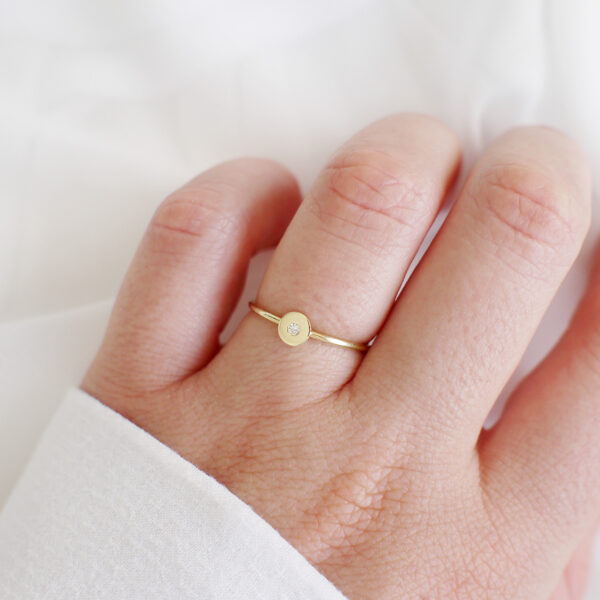 Mão feminina usando Anel de aro fino minimalista feito a mão em ouro 18k com diamante no centro sobre tecido branco