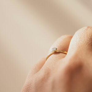 mão feminina usando anel de noivado minimalista de ouro 18k com diamante de 12p feito à mão