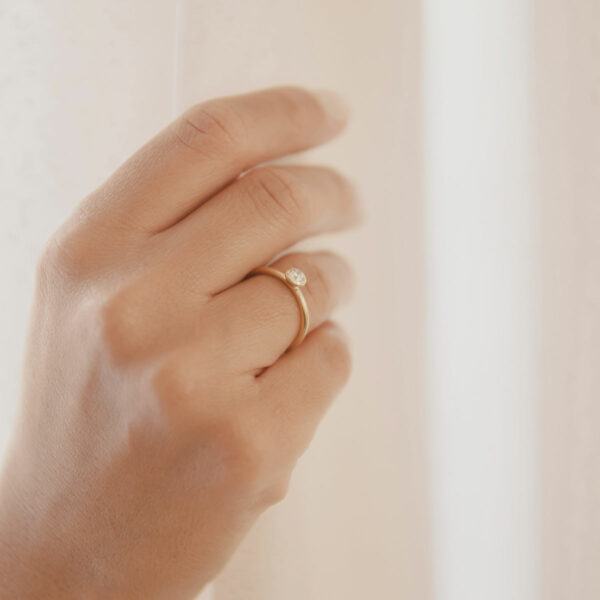 mão feminina usando anel de noivado minimalista de ouro 18k com diamante de 22p feito à mão