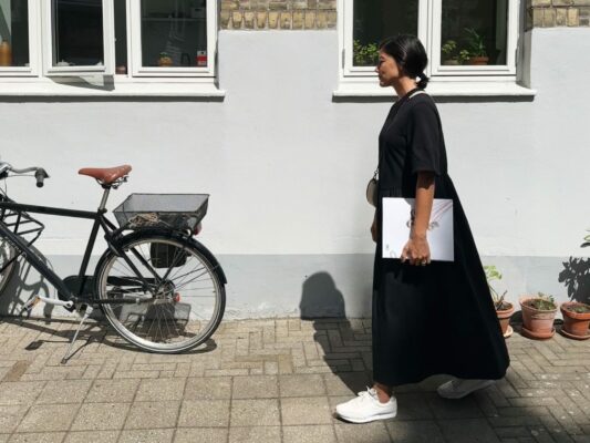 Lie passando em frente uma fachada de vestido preto perto de uma bicicleta retro preta