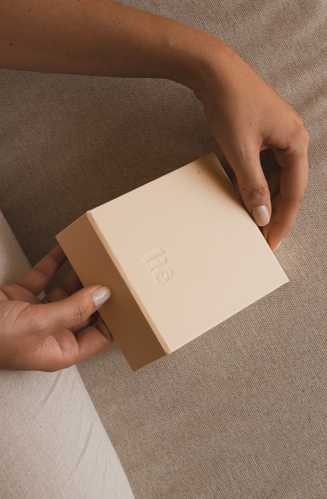Mãos de unha branca segurando a embalagem de joias, parte externa de papel da Joias Liê.