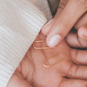 Mão feminina segurando Brinco minimalista fino feito a mão em ouro 18k em formato de anzol
