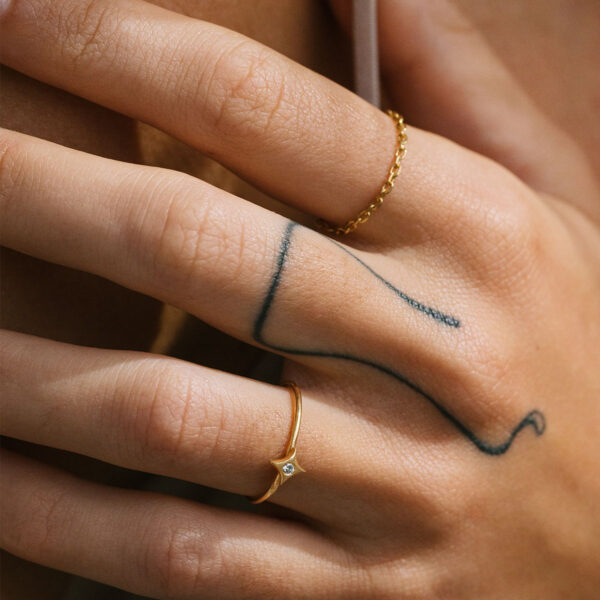 Mão feminina usando anel de corrente e anel com uma estrela e diamante feitos a mão em ouro 18k