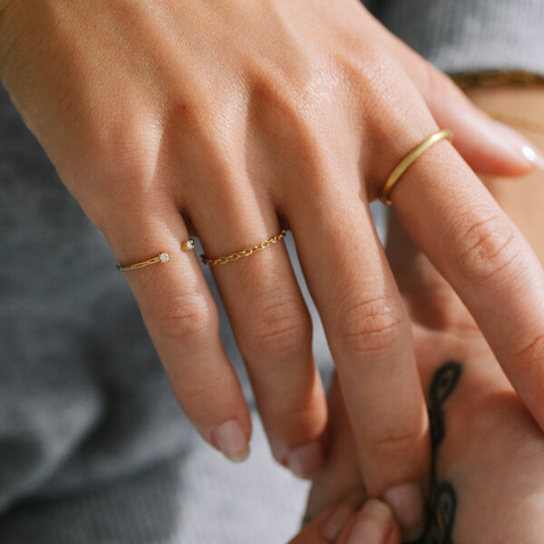 Mão feminina usando anel de corrente, anel aberto com dois diamantes e aliança redonda feitos a mão em ouro 18k