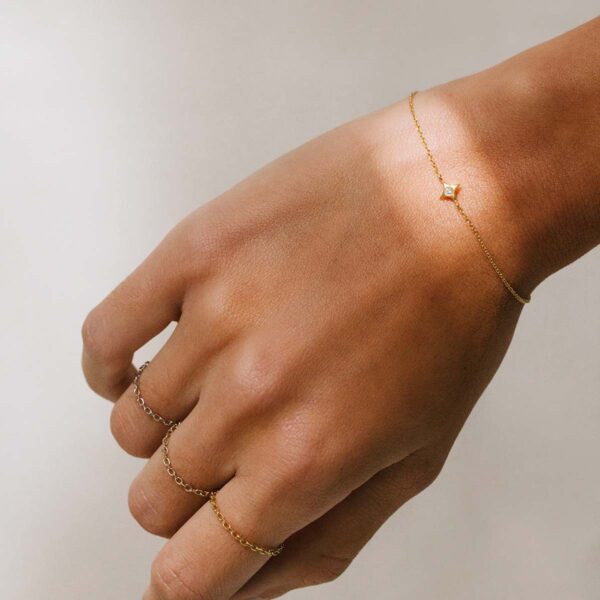Mulher usando Anéis minimalistas feitos a mão com correntes em diferentes tons de ouro 18k e pulseira com estrela e um diamante