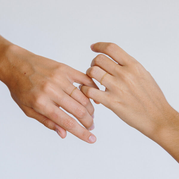 Mão entrelaçadas usando Anéis minimalistas feitos a mão com correntes em diferentes tons de ouro 18k