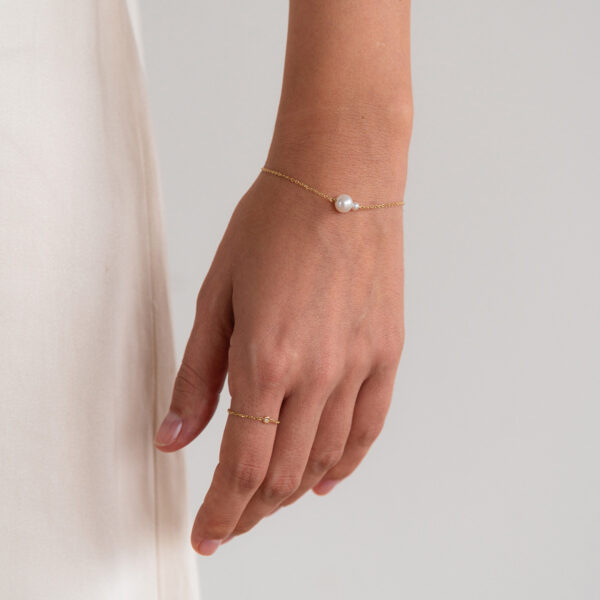 Mão feminina usando pulseira de ouro amarelo 18k e duas pérolas naturais e anel de ouro amarelo 18k com um diamante de 1 ponto